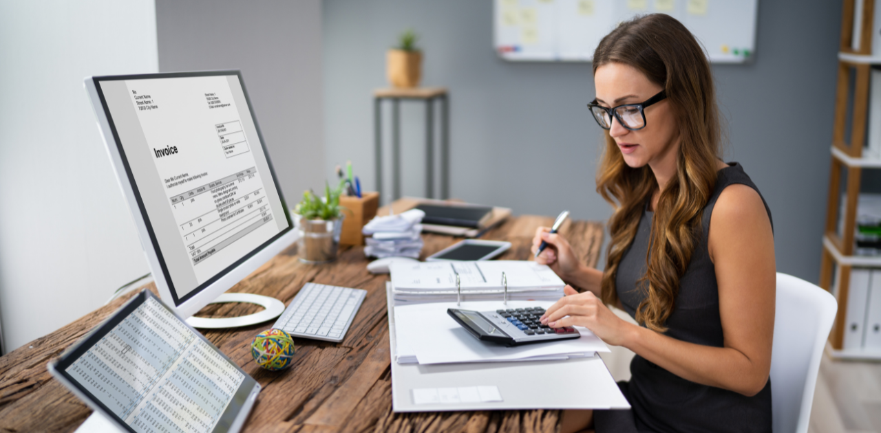 Person sitz an einem Schreibtisch mit Monitoren, Tastatur und Taschenrechner
