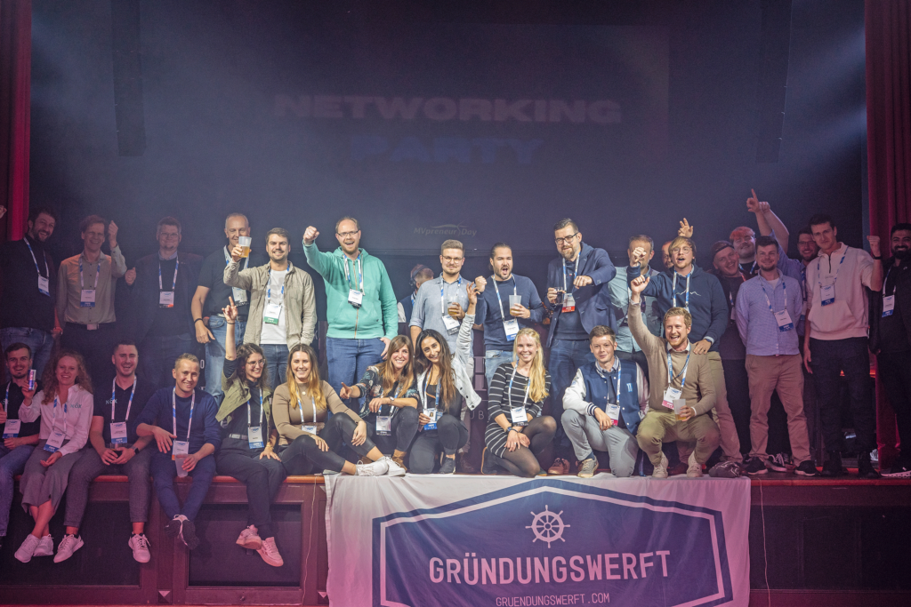 Eine Gruppe jubelnder Menschen auf der Bühne einer Gründungsveranstaltung in Rostock mit der Schrift Networking Party im Hintergrund