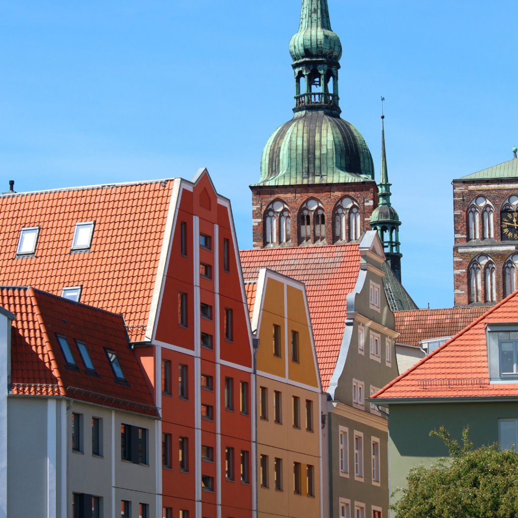 Farbenfrohe Häuserfassaden der Stralsunder Innenstadt, im Hintergrund die Kuppel Marienkrche bei blauem Himmel 