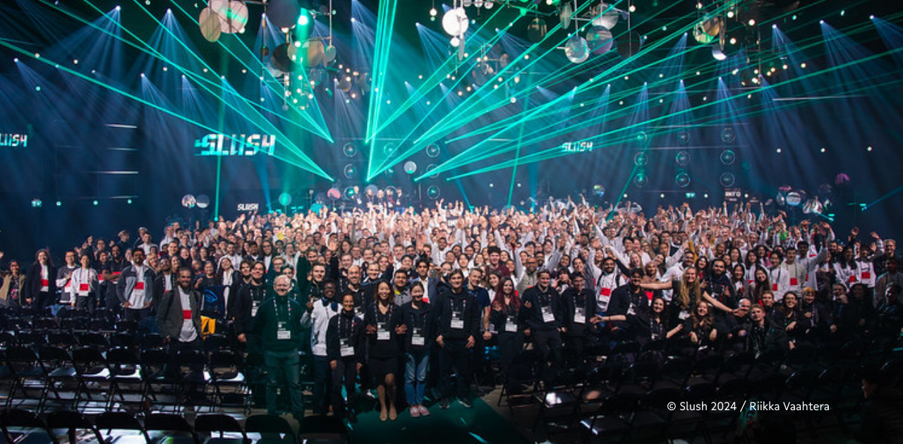 Teilnehmende posieren auf der Slush 2024 in Helsinki vor dem offiziellen Event-Banner.