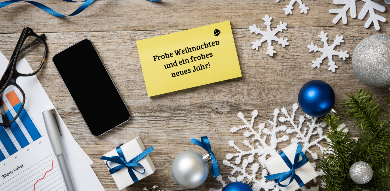 Selbstständige: Weihnachtlich dekorierter Schreibtisch mit Smartphone, Geschenken und Karte „Frohe Weihnachten und ein frohes neues Jahr!"
