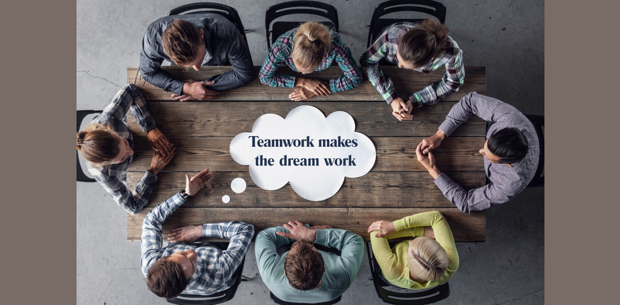 Acht Personen sitzen um einen Tisch und arbeiten gemeinsam an Ideen. In der Mitte steht: „Teamwork makes the dream work“.