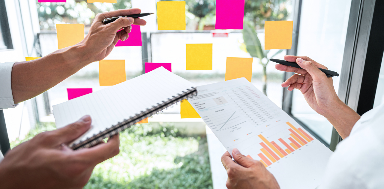 Hände mehrerer Personen, die gemeinsam über Diagramme, Notizen und Post‑its arbeiten – eine Team‑Situation, die strukturelle Faktoren des Gender Pay Gap 2026 symbolisiert.