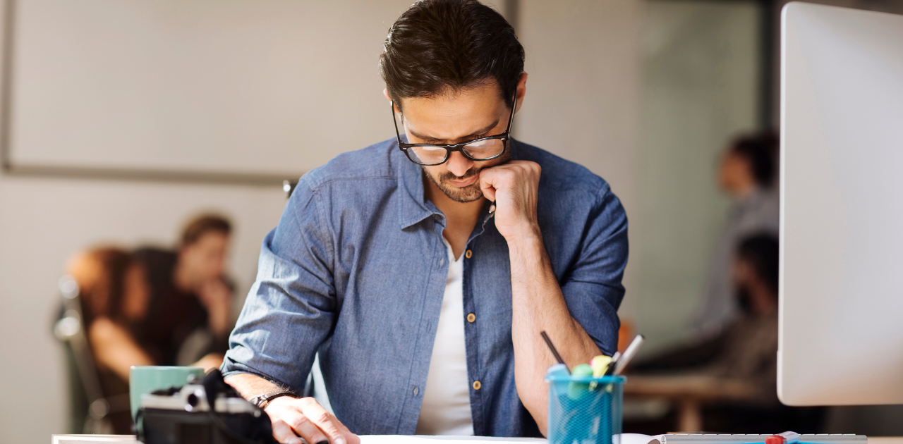 Person an einem Schreibtisch blickt nachdenklich auf Papiere, die vor ihm liegen