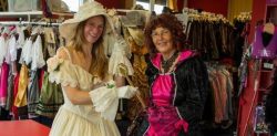Zwei Personen in historischen Kostümen stehen im Kostümfundus von Klamöttchen, umgeben von zahlreichen Kleidern und Accessoires im Rahmen der Unternehmensnachfolge im Kostümverleih.