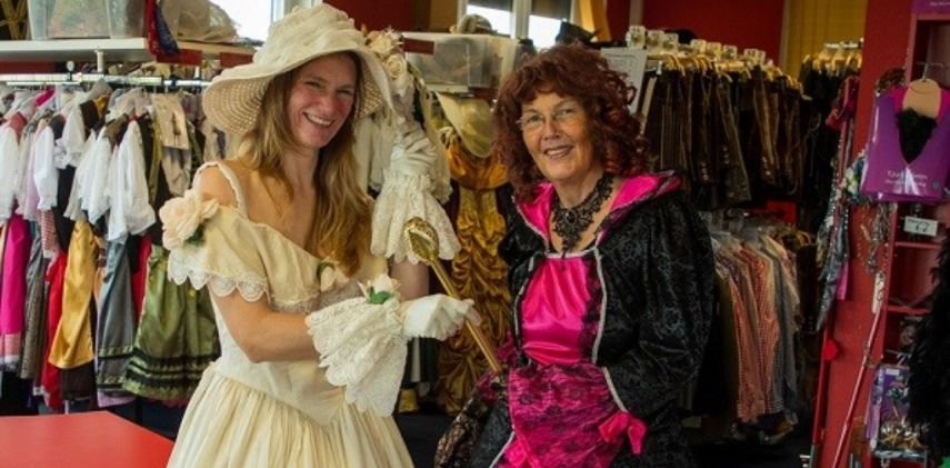 Zwei Personen in historischen Kostümen stehen im Kostümfundus von Klamöttchen, umgeben von zahlreichen Kleidern und Accessoires im Rahmen der Unternehmensnachfolge im Kostümverleih.