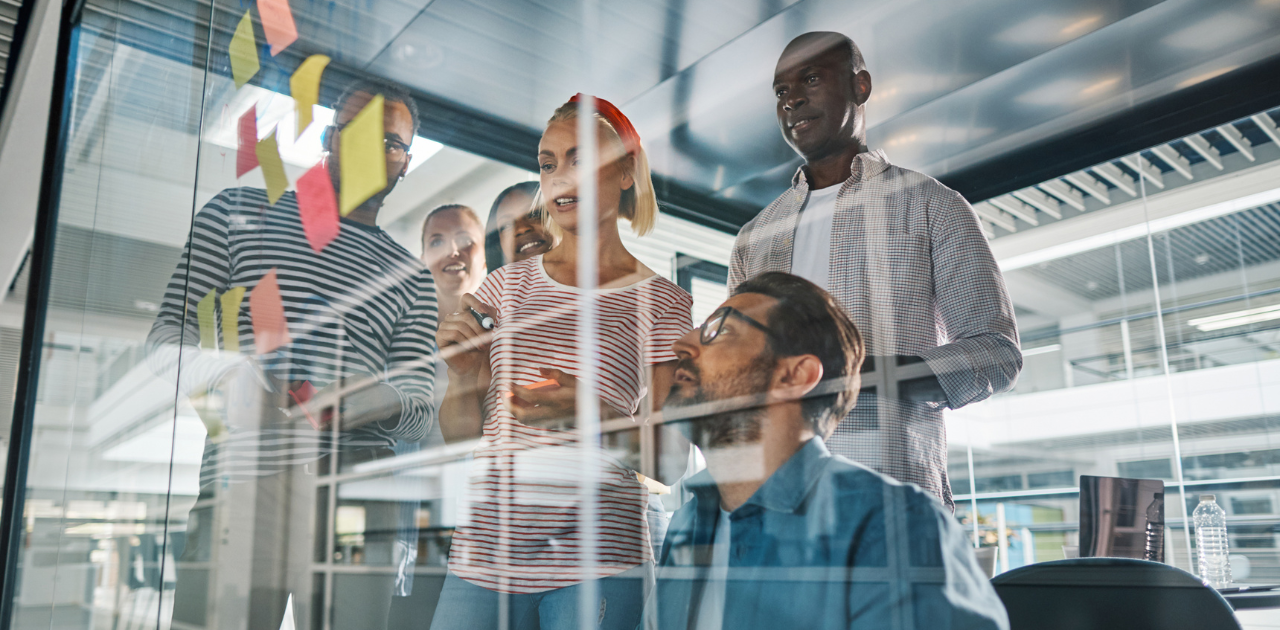 Mehrere Personen stehen vor einer Glaswand, auf der mehrere Post-its kleben