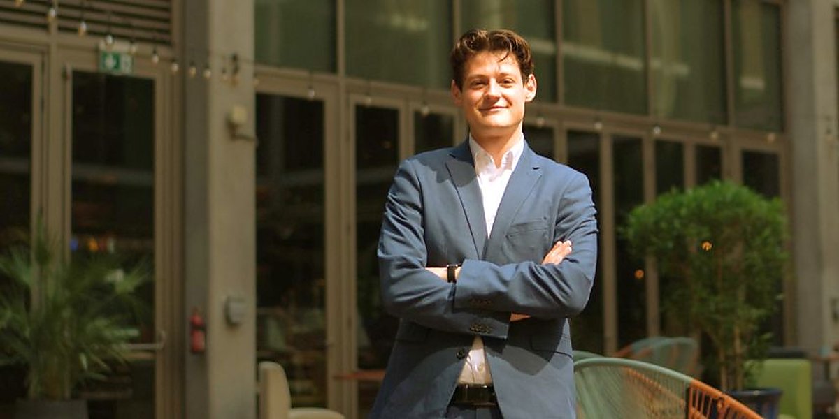 Person steht mit verschränkten Armen vor einem modernen Gebäude, passend zum Thema Wasserstoff‑Infrastruktur und Unternehmensgründung.