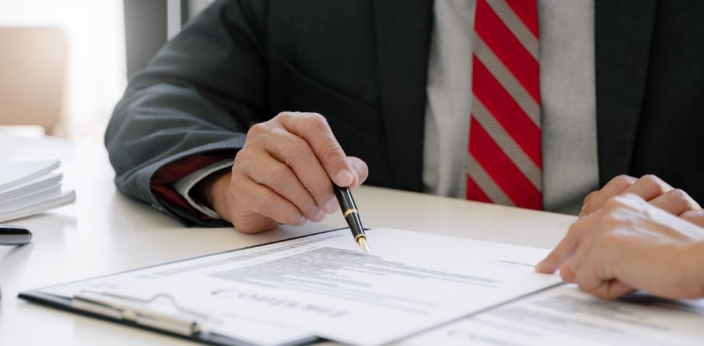 Symbolbild für AGB: Eine Person zeigt mit einem Stift auf eine Seite mit Text, die vor ihr liegt