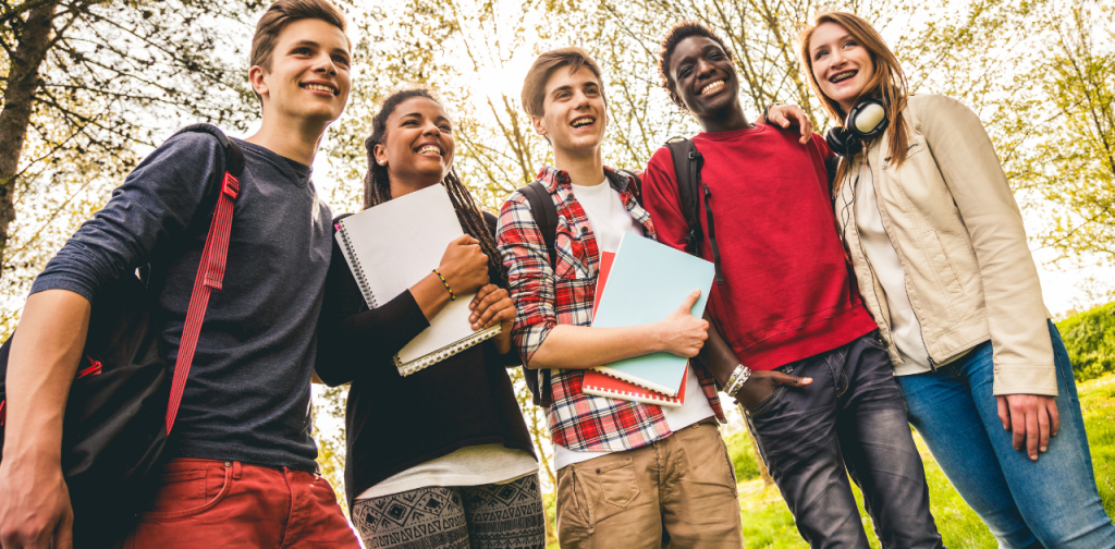 Fünf Schüler:innen mit Notizbüchern im Park, lachend und im Gespräch – Gründerpreis für Schüler