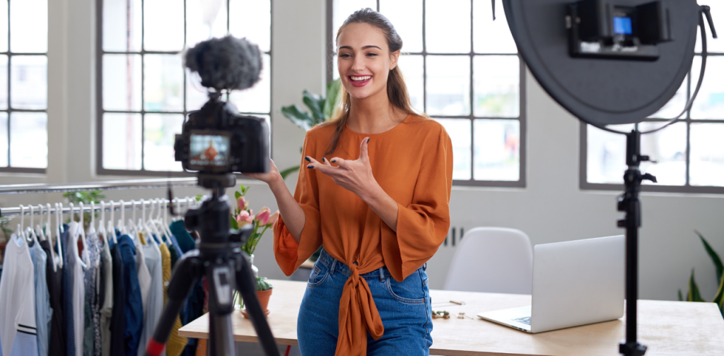 Influencerin steht vor Kamera und spricht in Mikrofon, während sie einen Vlog aufnimmt – professionelles Setting mit Ringlicht und Laptop im Hintergrund.