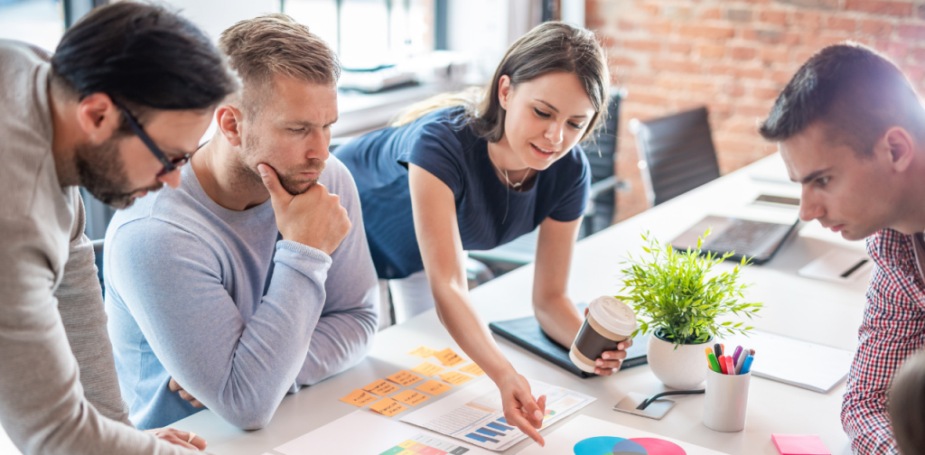4 Personen an einem Tisch diskutieren über Grafiken, die auf dem Tisch liegen