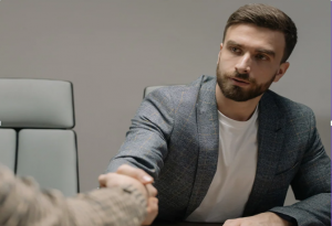eine jüngere Person reicht einer anderen Person über den Tisch hinweg die Hand