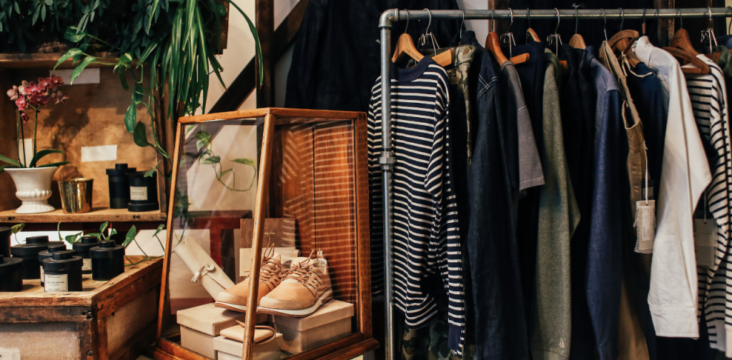Blick in einen kleinen Laden mit Kleidungsstücken auf einer Kleiderstange und Schuhen und mehr in einer Vitrine