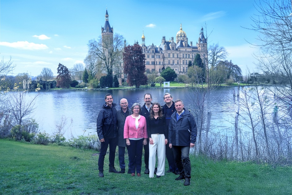 Gruppe von Menschen vor einem Schloss am See – Symbolbild für erfolgreiche Unternehmensnachfolge im Handwerk
