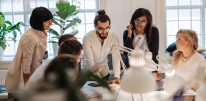 eine Personengruppe beugt sich über einen Tisch und diskutiert miteinander, eventuell über das Thema Stakeholder