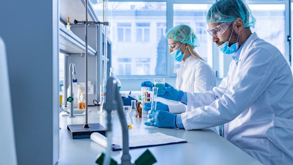 Zwei Personen arbeiten an einem Labortisch, sie tragen Mundschutz