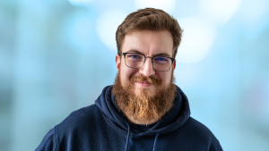 Porträt von Simon Glowik vor blauem Hintergrund. Der Gründer von NordFlux blickt in die Kamera. Das Bild dient als Titelbild einer Gründerstory über den Aufbau seines Unternehmens in Wismar.